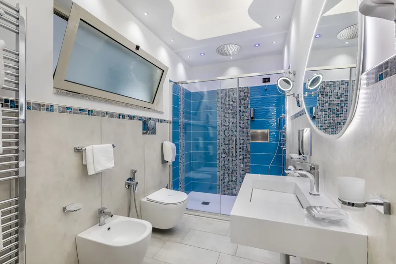 Bagno con doccia a piastrelle blu, lavabo bianco e specchio illuminato