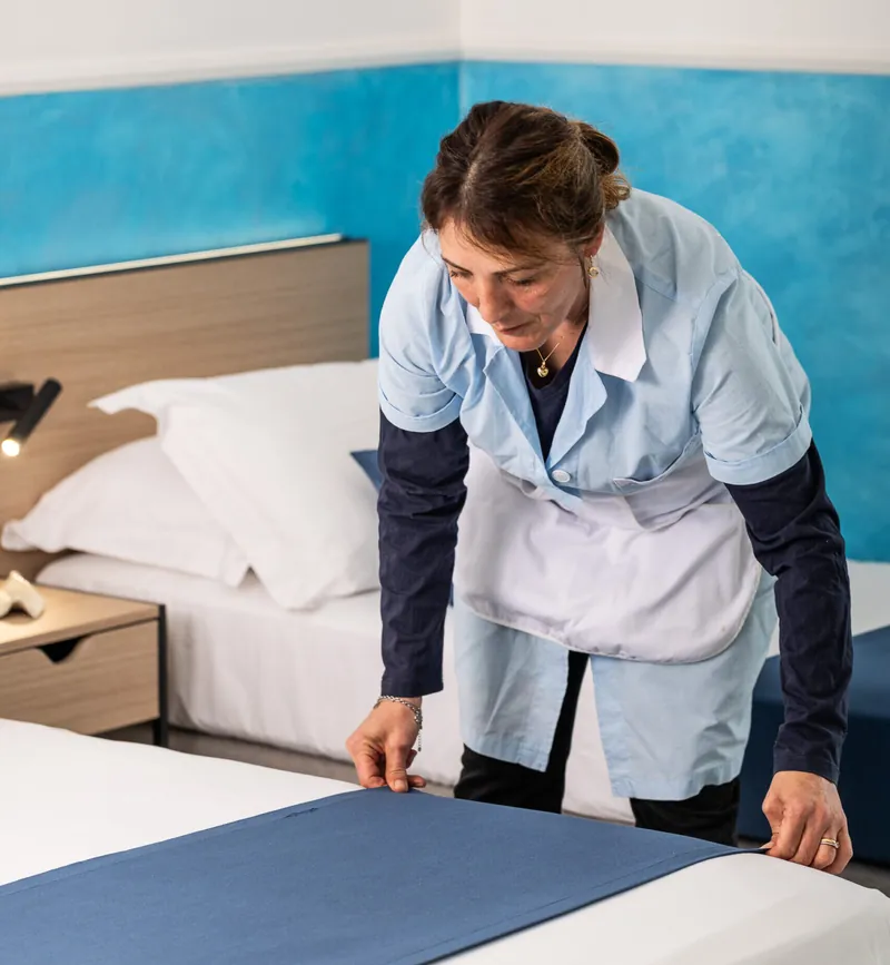 Cameriera che rifà il letto con il copriletto blu