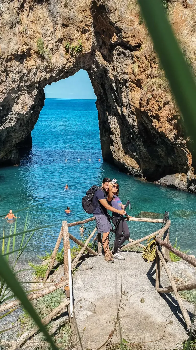 Coppia sulla scogliera davanti all'arco di roccia sul mare